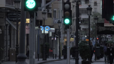 Calle-Nocturna-Con-Tiendas,-Gente-Caminando-Y-Tráfico-De-Transporte-En-España.