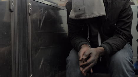Homeless-man-in-subway-train-hiding-face-under-the-hood