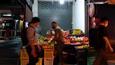 Man-buying-some-fruits-from-a-sidewalk-fruit-vendor-in-Bangkok-during-the-night,-Thailand