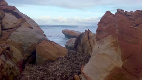 Walk-through-video-over-rocky-formation-on-the-beach,-sea-waves-are-crashing-to-the-coastline-shore