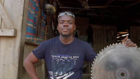 African-Saw-Metal-Worker-Smiles-at-Close-Up-Camera-in-Wooden-Workshop-in-Ghana