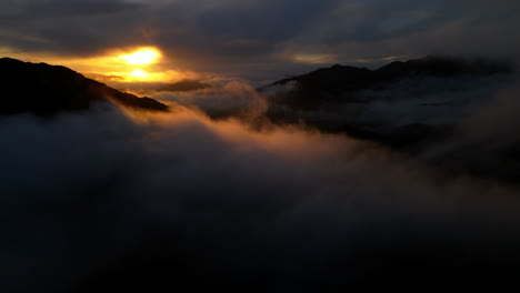 Sun-rising-over-cloud-shrouded-valley-and-mountains-with-slow-camera-rise