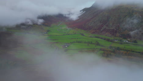 Fliegen-über-Niedrigen-Wolken-Mit-Blick-Auf-Ein-Grünes-Tal,-Umgeben-Von-Bergen,-Die-Von-Wolken-Umhüllt-Sind
