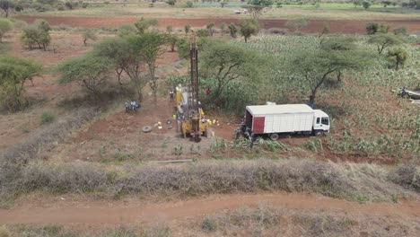 African-workers-drill-water-well-with-mechanic-bore,-freshwater-search-for-poor-region,-aerial