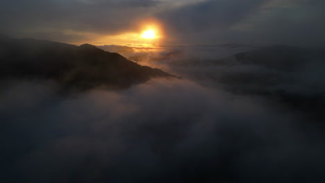 Sonnenaufgang-über-Wolkenverhangenen-Bergsilhouetten-Mit-Langsamem-Rückzug-In-Dünne-Wolken