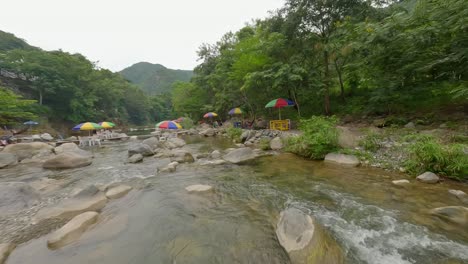 FPV-drone-flying-over-Rio-Bani-River-with-open-umbrellas-and-tables-with-chairs-on-river-rocks