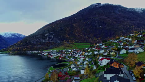 Zoom-in-aerial-shot-of-a-town-situated-near-a-lake-in-Norway-mountain-summits-in-the-background