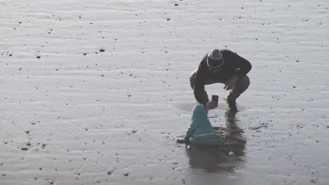 Ein-Vater-Mit-Kind-Am-Strand,-Der-Im-Nassen-Sand-Spielt-Und-Fotos-Macht