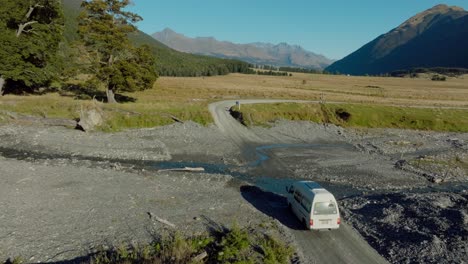 Aerial-drone-view-of-white-tourist-campervan-splashing-through-shallow-river-crossing-in-Dart-Valley,-Glenorchy,-South-Island-of-New-Zealand-Aotearoa
