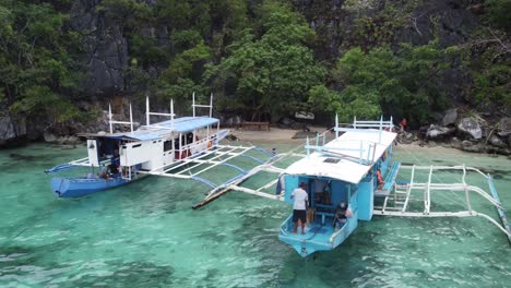 Island-hopping-tour-boats-and-people-having-lunch-on-skeleton-wreck-beach,-Coron