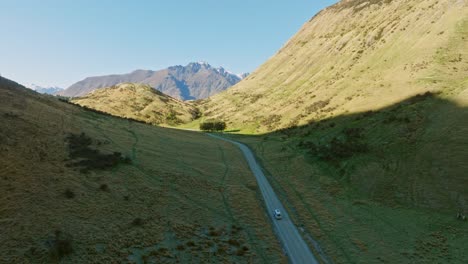 Aerial-drone-view-of-campervan-traveling-on-remote-road-through-wild-and-rugged-alpine-mountainous-landscape-near-Queenstown-in-Otago,-South-Island-of-New-Zealand-Aotearoa