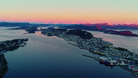 Aerial-shot-of-city-of-Norway-Aalesund-during-the-twilight-with-orange-hue-on-the-snow-capped-mountains
