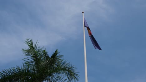 Bandera-De-La-ASEAN-Ondeando-Mientras-La-Cámara-Se-Inclina-Un-Poco,-Una-Palmera-A-La-Izquierda-Con-Un-Hermoso-Cielo-Azul-Y-Algunas-Nubes