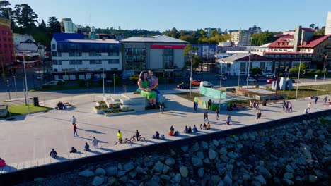 Families-and-people-walking,-taking-photos,-and-enjoying-the-sunny-day-around-the-sculpture-‘Sentados-frente-al-mar’-in-Puerto-Montt,-Chile