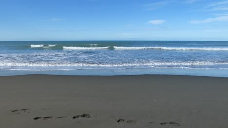Small-waves-roll-into-beach-with-footprints-in-sand-on-a-sunny-day---Pegasus-Bay,-New-Zealand
