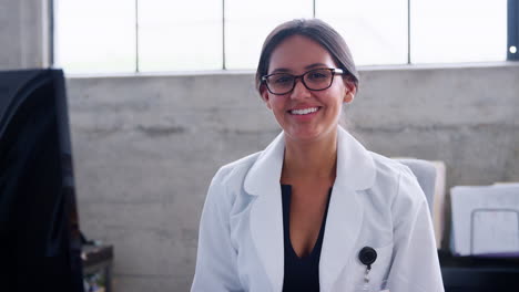 Young-female-doctor-in-glasses-smiling-to-camera-in-office