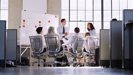 Young-male-manager-standing-by-a-whiteboard-at-a-meeting