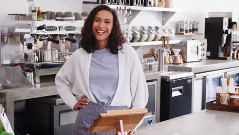 Mixed-race-female-coffee-shop-owner-smiling-behind-counter