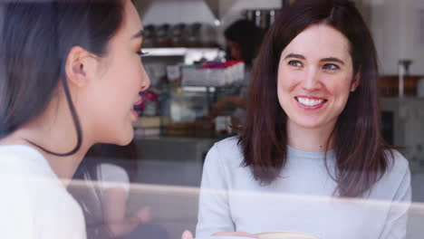 Female-friends-laughing-in-coffee-shop,-seen-through-window
