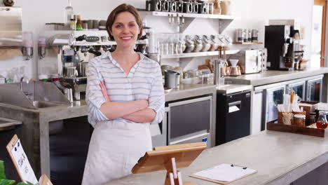 Female-coffee-shop-owner-leaning-on-counter-at-coffee-shop