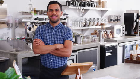 Young-male-coffee-shop-owner-crossing-arms-behind-counter
