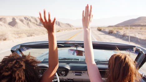 Two-female-friends-raise-hands-driving-in-an-open-top-car