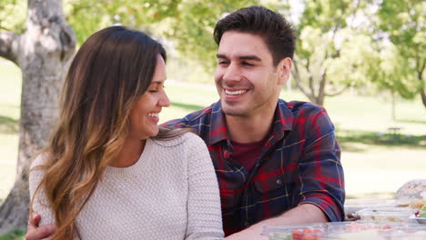 Young-smiling-couple-embracing-at-a-table-in-a-park