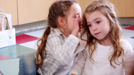 Two-elementary-schoolgirls-whispering-in-class