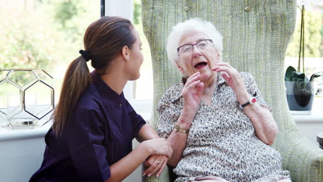 Senior-Woman-Sitting-In-Chair-And-Talking-With-Nurse-In-Retirement-Home