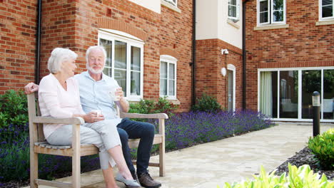 Retired-Couple-Sitting-On-Bench-With-Hot-Drink-In-Assisted-Living-Facility