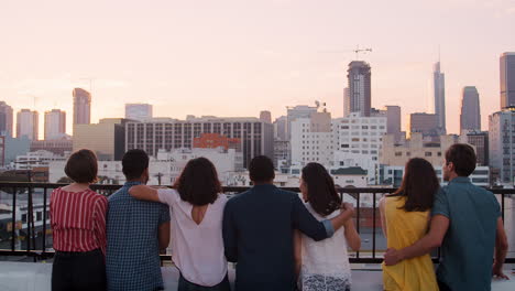 Rear-View-Of-Friends-Gathered-On-Rooftop-Terrace-Looking-Out-Over-City-Skyline