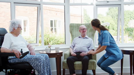 Male-And-Female-Residents-Sitting-In-Chair-And-Talking-With-Nurse-In-Retirement-Home