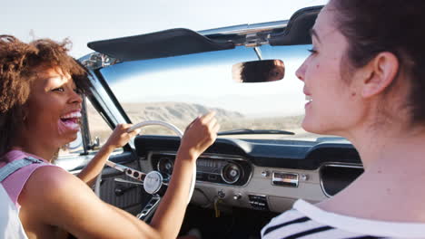 Two-female-friends-driving-on-a-desert-road-in-a-classic-car