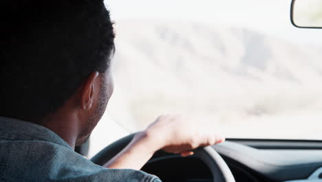 Young-black-man-driving-car-and-talking,-over-shoulder-view