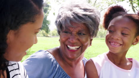 Grandmother-With-Adult-Daughter-And-Granddaughter-Relaxing-In-Park