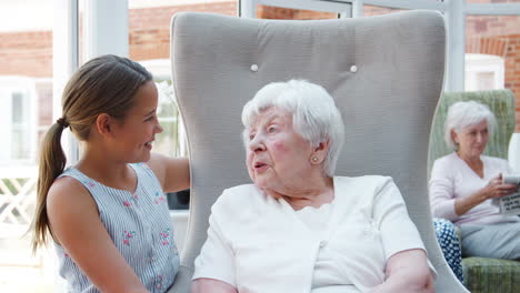 Granddaughter-Sitting-And-Talking-With-Grandmother-During-Visit-To-Retirement-Home