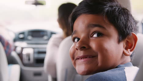 Niño-Sonriente-Viajando-En-La-Parte-Trasera-De-Un-Auto-Con-Sus-Padres