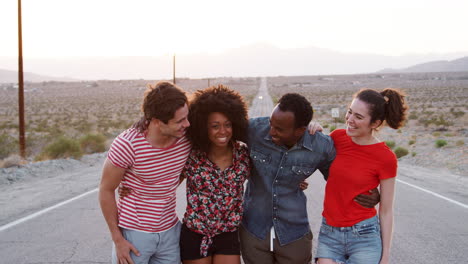 Four-happy-friends-standing-on-a-desert-highway,-close-up