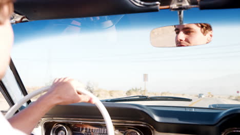 Young-white-man-driving-an-open-top-car,-face-seen-in-mirror