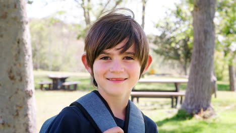 Slow-Motion-Portrait-Of-Young-Boy-With-Backpack-In-Park-Smiling-At-Camera