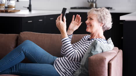 Senior-woman-video-calling-with-smartphone-on-couch-at-home