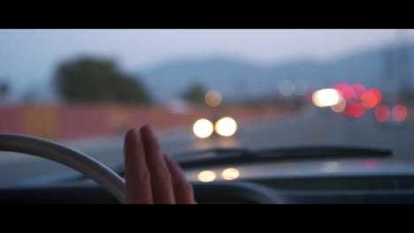 Man-tapping-steering-wheel-as-he-drives,-with-bokeh-lights