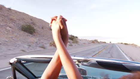 Young-black-couple-in-open-top-car-holding-hands-in-the-air