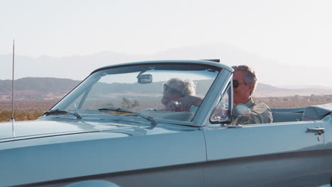 Smiling-senior-couple-driving-classic-convertible-on-highway