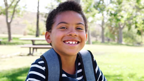 Slow-Motion-Portrait-Of-Young-Boy-With-Backpack-In-Park-Smiling-At-Camera