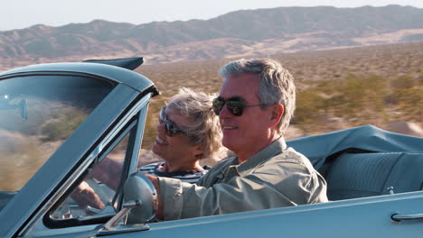 Senior-couple-driving-in-open-top-car-on-a-desert-highway