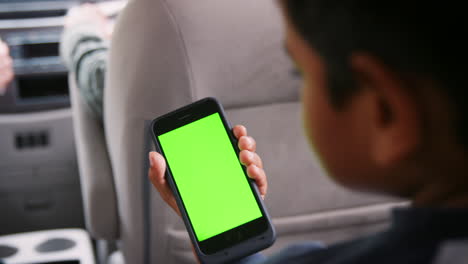 Young-boy-sitting-in-a-back-of-the-car-using-a-smartphone