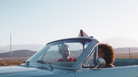 Laughing-female-friends-driving-in-convertible-on-a-highway