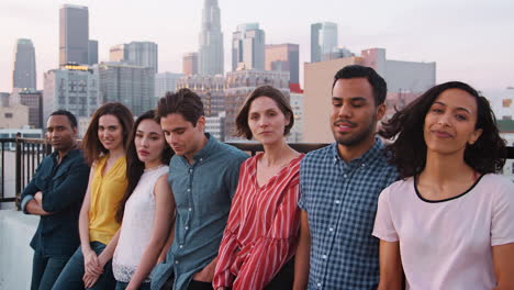 Portrait-Of-Friends-Standing-In-A-Line-Gathered-On-Rooftop-Terrace-With-City-Skyline-In-Background