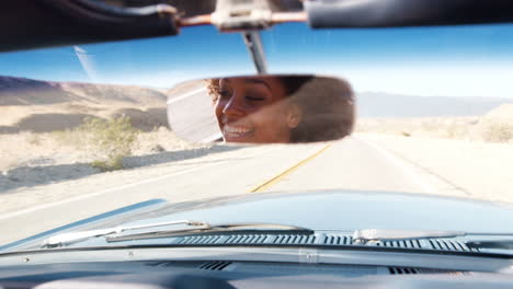 Young-woman-driving-open-top-car,-seen-in-rear-view-mirror